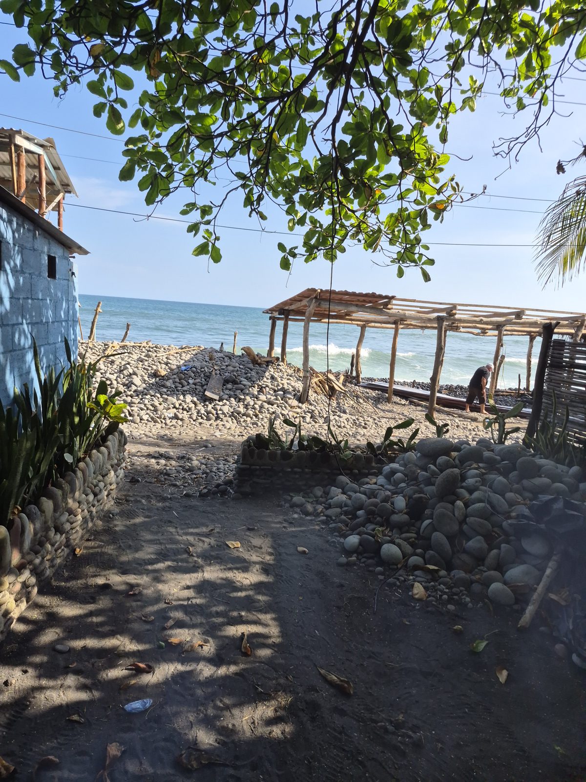 Beachfront wooden pergola on black volcanic sand with the Pacific Ocean and palm trees