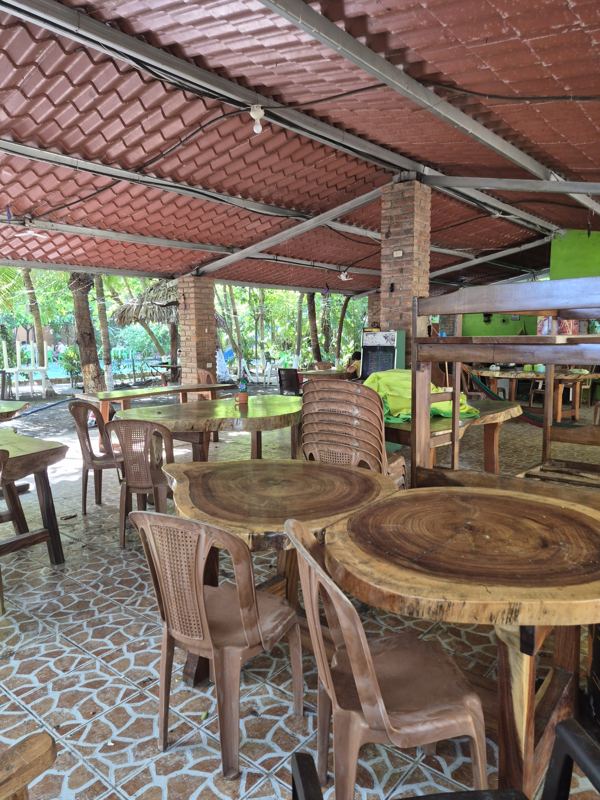 Open-air restaurant pavilion with wooden tables and chairs under a tiled roof